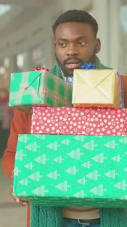Festive Scene with Crowded Shopping Corridor Man Struggles to Carry Colorful Packages in Busy Mall