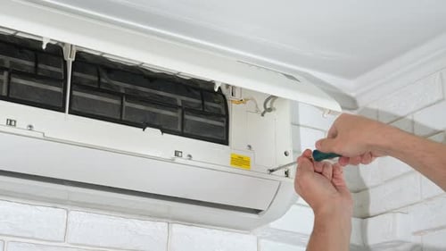 Hands Repairing Air Conditioner with Screwdriver Indoors