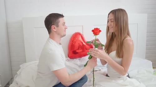 Man Gives Red Rose to Woman on Bed
