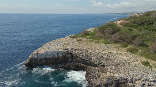Aerial view of a rocky coastal cliff surrounded by the vast blue sea, with waves crashing at its bas