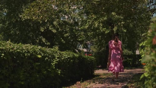 Gentle Woman on Sunny Walk Woman in Pink Dress Explores Garden Path Elegant Woman in Flowing Attire