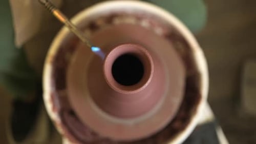 Focus superficiel regardant vers le bas sur un vase en argile tournant sur un tour de poterie émaillé avec une torche au propane