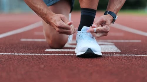 Runner ties his sports shoes to start training on running track, close-up