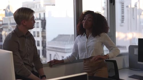Coworkers discussing near window in modern office