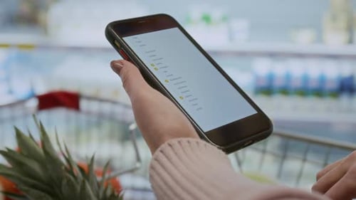 Woman Holding Phone with Shopping List on Screen in Supermarket
