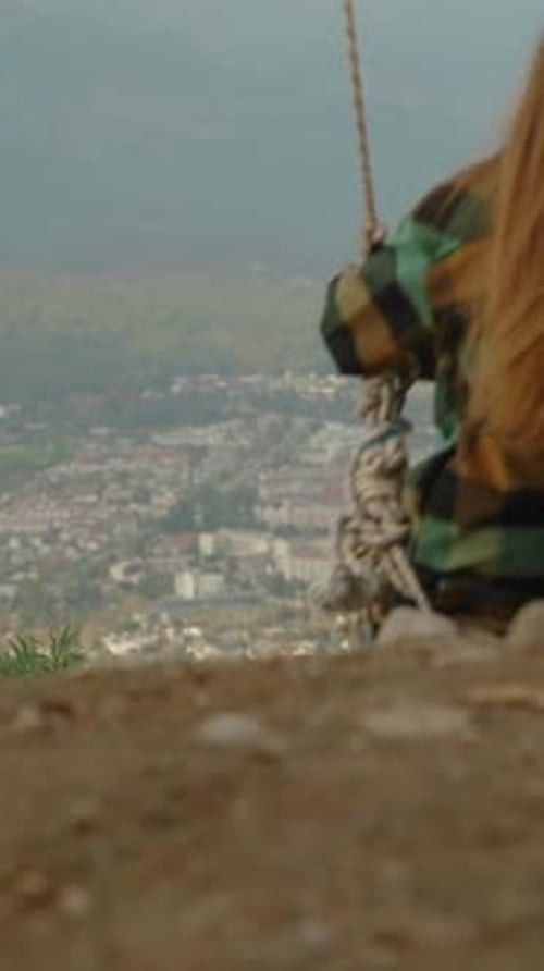 Girl on Swing Above the City in Mountains