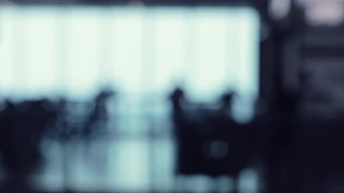 A defocused shot of many silhouettes of people walking around in a food court office building.