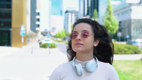 Young Joyful Woman Student in Sunglasses Walking in City and Looking Around