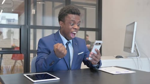 Young African Businessman Excited for Win on Phone at Workplace