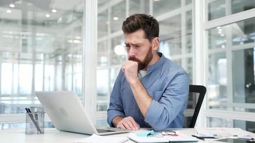 Unhealthy businessman coughing while sitting at workplace at desk in a modern business office. Sick
