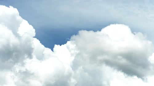 Cumulus clouds move against a clear blue sky. A white fluffy cloud is flying rapidly through the air