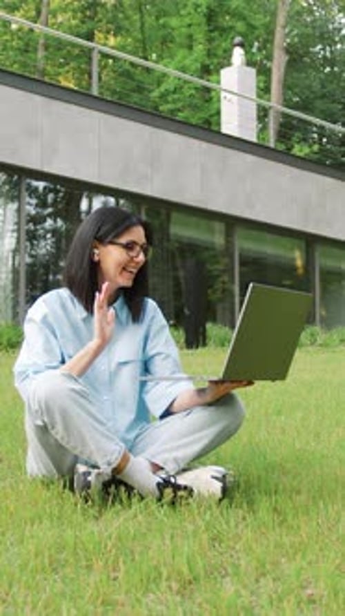 Beautiful Young Woman Sitting in a City Park Talking on the Phone While Typing on a Laptop Concept