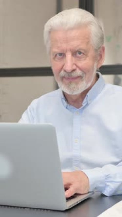 Senior Businessman Smiling at Camera while Working on Laptop in Office