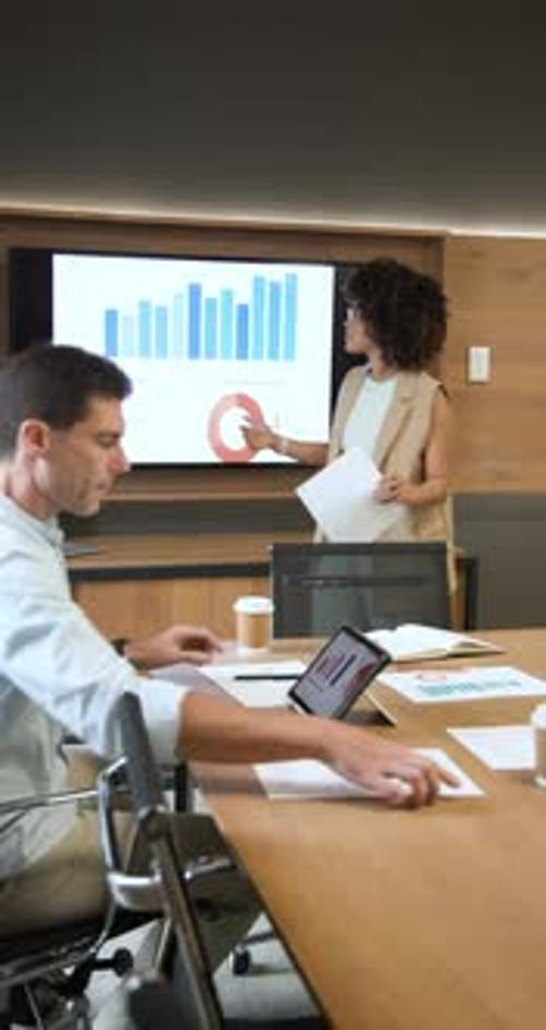 Diverse coworkers responding to tablet charts at conference table exchanging printouts highfiving