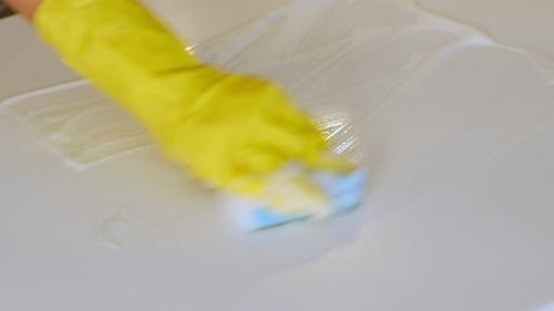 Gloved Hand Cleans Countertop with Sponge and Soap