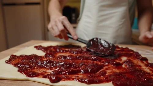 Using a Black Spatula to Spread Cherry Jam on Dough, Ensuring the Filling Covers the Entire Surface.