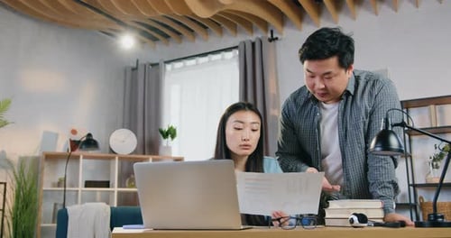 Attractive asian man standing near woman and helping with university hometask on computer