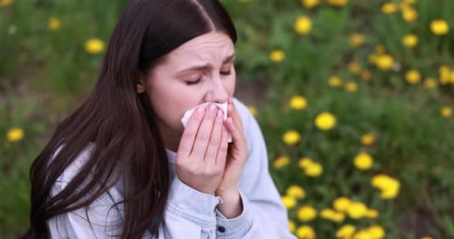 Seasonal allergy. Woman sneezing in park on spring day