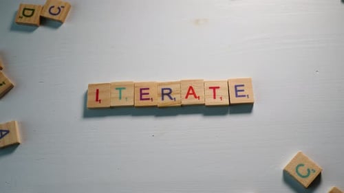 Alguien deletrea Iterate con letras de madera sobre un fondo blanco con otras letras dispersas. Dibuja