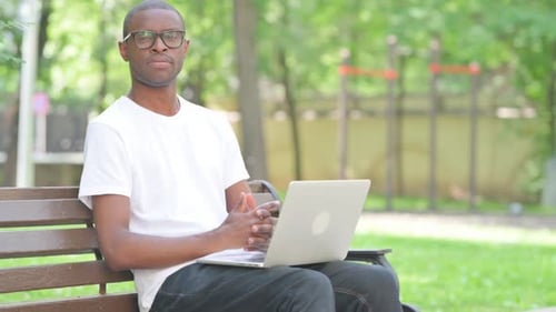 Young Adult Using Laptop Computer on Park Bench