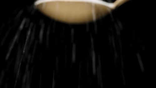 Sugar is poured from above on a golden spoon. Dolly slider extreme close-up. Laowa Probe