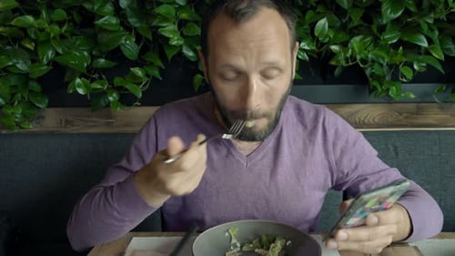 Young Man with Smartphone Eating Salad in Restaurant 30s