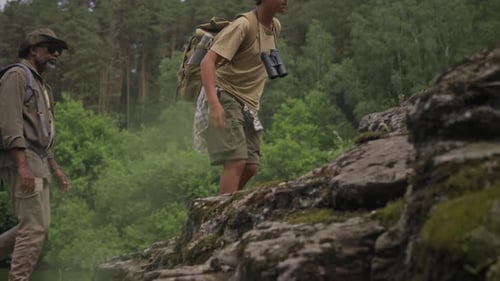 Black Grandfather and Grandson with Backpacks Climbing up Stony Hill