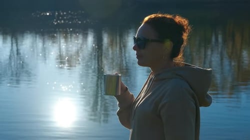Woman Drinking Hot Tea From a Mug By the Lake at Sunset