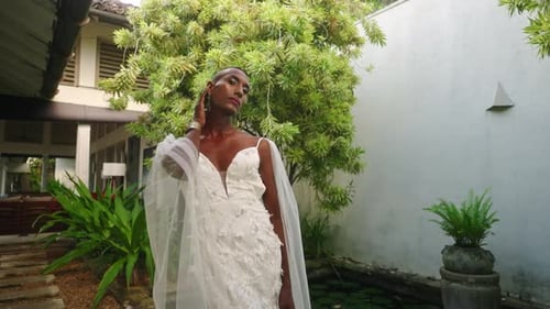 LGBTQ Black Person Posing As Model in Tropical Garden Near Water Lily Pond in White Wedding Dress