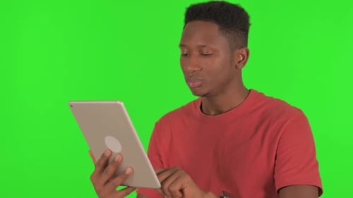 Casual African Man Using Digital Tablet on Green Background
