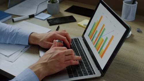 Closeup Businessman Hands Typing Laptop Computer with Graphics on Screen in Office