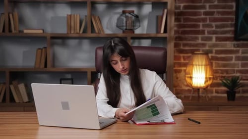 Business Woman Working on Documents While Looking at Laptop in Modern Office Setup