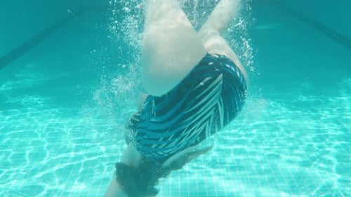 Blue swimming pool, underwater shooting, sunny day. Chubby young woman somersaults in the water. Slo