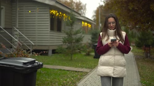Woman Using Smartphone While Walking on Suburban Street