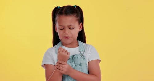 Child, girl and wrist pain or hand on studio background for sprained muscle
