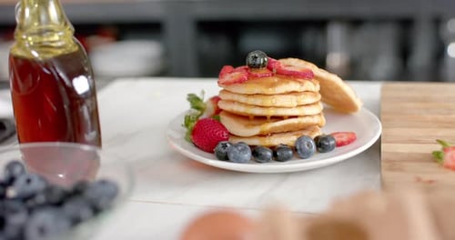 Close up of pancakes with fruits and honey in kitchen, slow motion