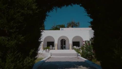 Entrance of a white building passing through a green bush arch.