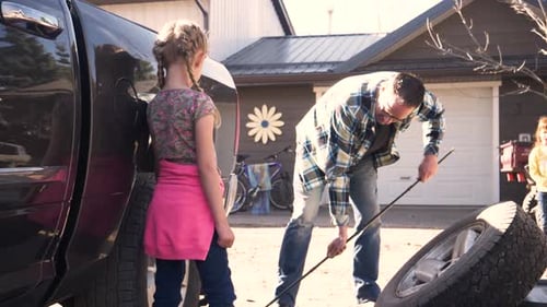 Man Working on Tire with Two Young Girls