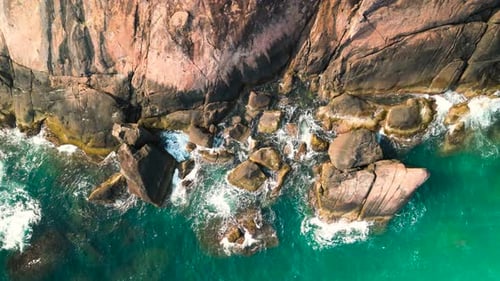 Aerial View Capturing Turquoise Ocean Waves Crashing Against Jagged Rocky Shoreline Generating
