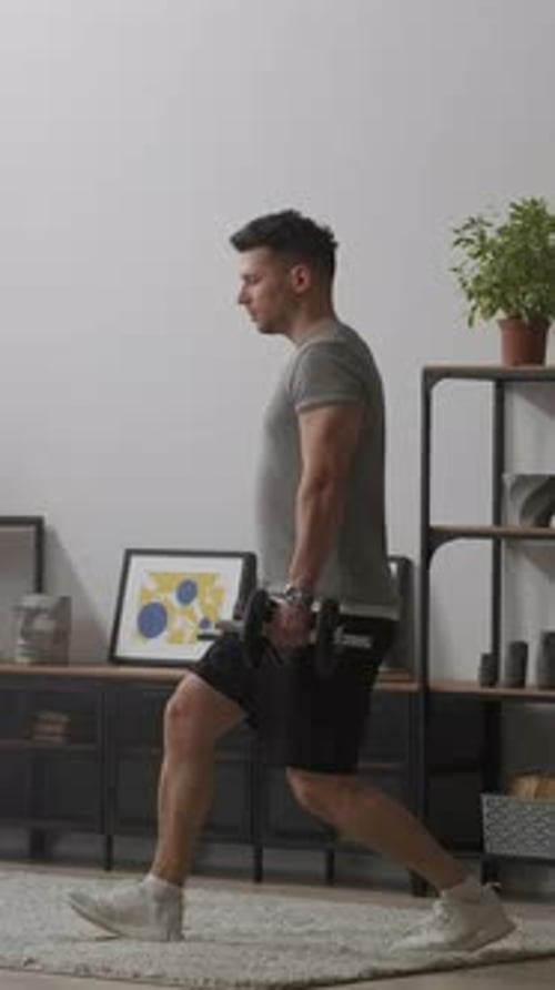 Focused Man Performing Dumbbell Lunge Exercise at Home Demonstrating Proper Posture Balance and