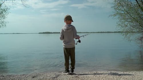 View from the back of a boy fishing on the river bank.
