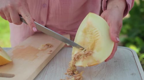 Femme caucasienne en gros plan grattant des graines de melon avec un couteau sur une planche à découper, table de jardin extérieure