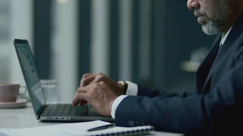 Senior Businessman in Formal Suit Typing on Laptop at Cafe Table