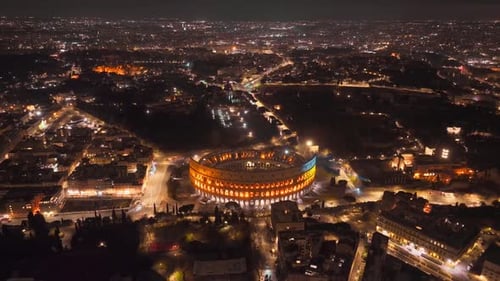 Aerial View of Colosseum in Roma Italy at NIght. Ancient Landmark and Streets in Lights, Drone Shot