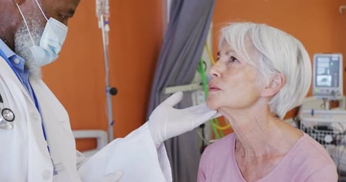 African american male doctor examining the neck of senior caucasian female patient at hospital