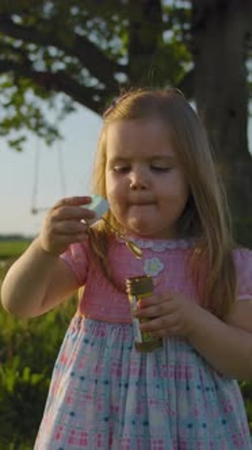 Vertical of Front View of Little Girl in Blows Soap Bubbles