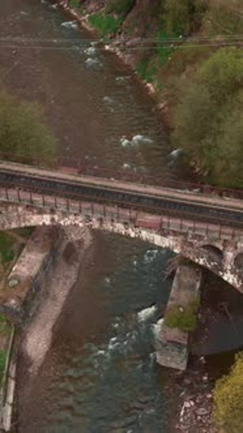 Aerial view of railroad viaduct bridge over river in mountains. Vertical video