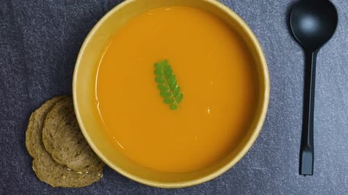 Warm pumpkin soup nestled in ceramic bowl, green herb garnish, crusty bread