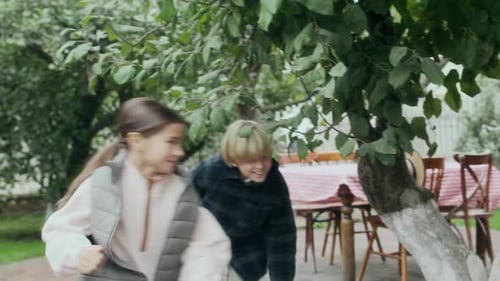 Kids Playing Catch Up Game around Leafe Tree in Lush Garden