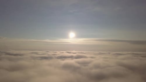 Drone Flying Through Clouds with Sun Above